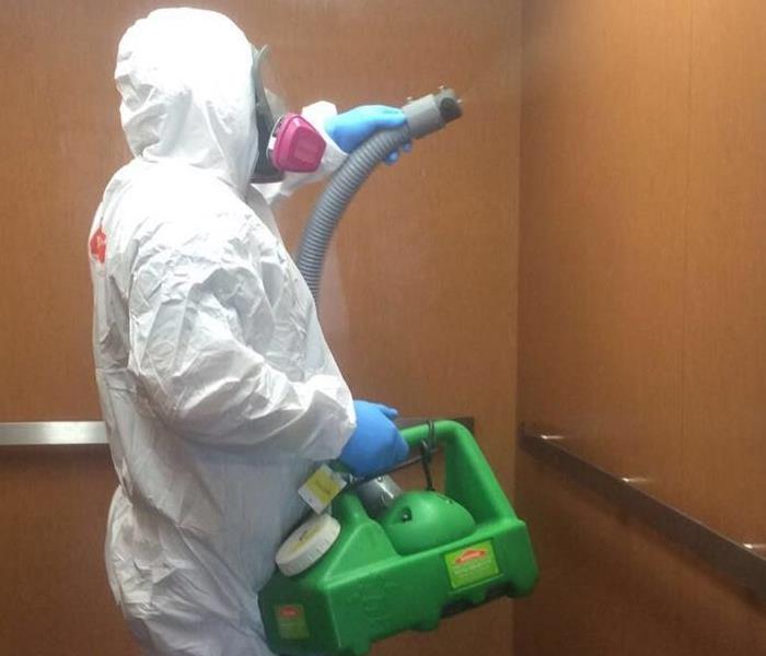 A person in full PPE fogging the inside of an elevator