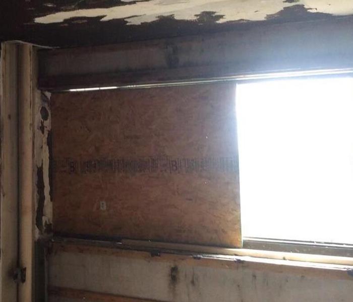 A room with fire damaged wall & ceiling.  A plywood board up up on half of the window